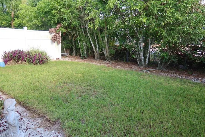 Expansive grassy lawn bordered by mature trees and a white privacy fence