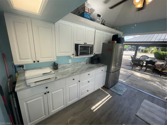 Kitchen featuring white cabinetry, lofted ceiling, light stone countertops, a ceiling fan, and refrigerator