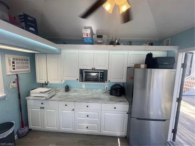 Kitchen featuring refrigerator, light countertops, white cabinets, ornamental molding, and dark wood finished floors