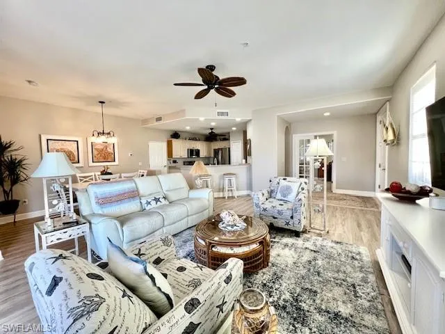 Living area with visible vents, ceiling fan with notable chandelier, baseboards, and light wood-type flooring