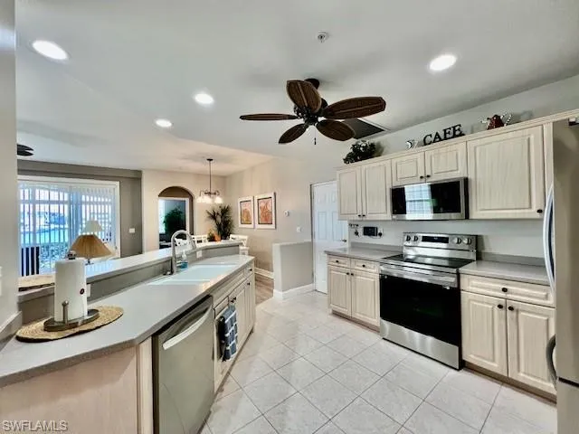 Kitchen featuring light countertops, light tile patterned floors, stainless steel appliances, ceiling fan with notable chandelier, and a sink