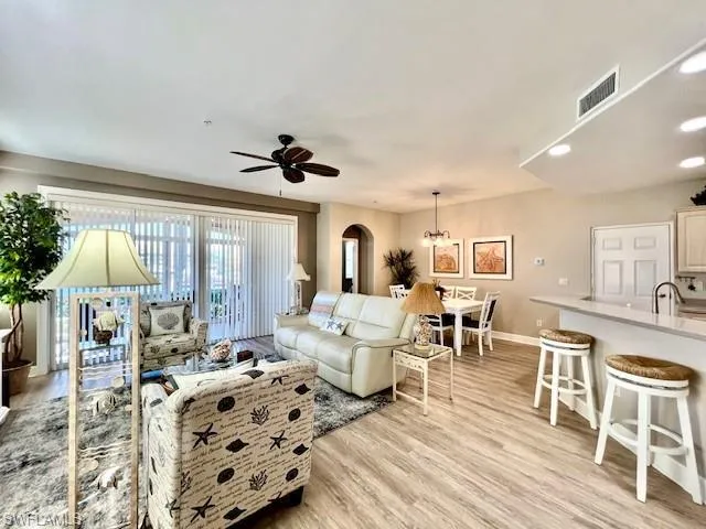 Living room with baseboards, arched walkways, light wood finished floors, visible vents, and a ceiling fan