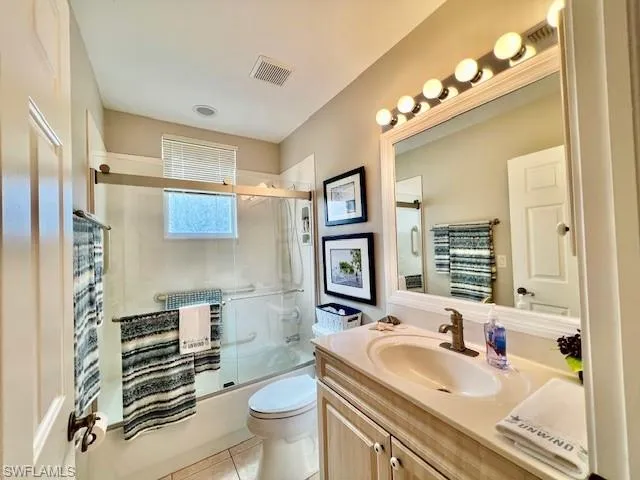 Bathroom with tile patterned flooring, vanity, toilet, bath / shower combo with glass door, and visible vents