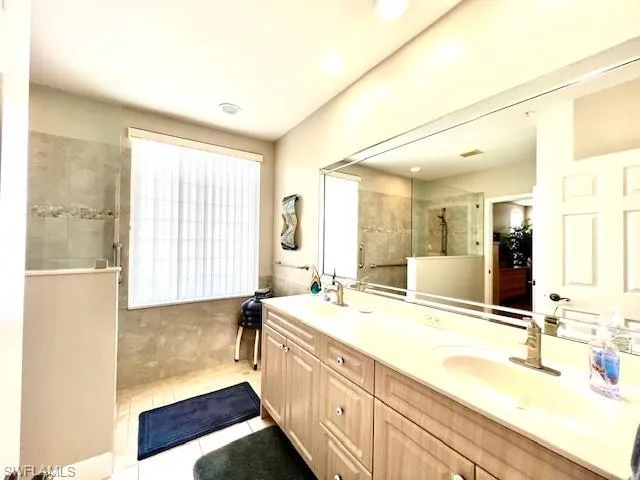 Full bath featuring tile patterned floors, a sink, double vanity, and a walk in shower