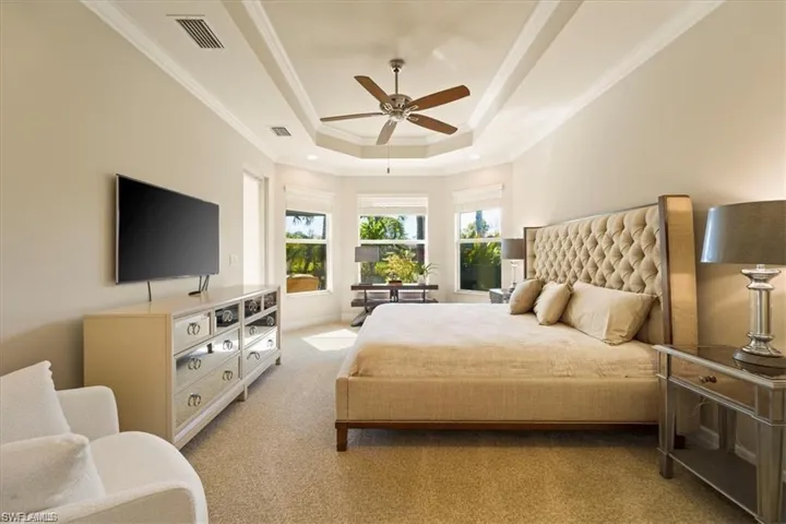Carpeted bedroom with a raised ceiling, ornamental molding, and a ceiling fan