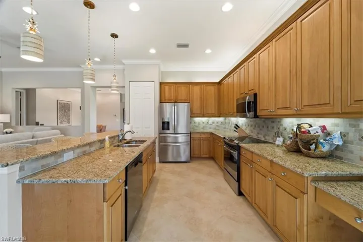 Kitchen featuring appliances with stainless steel finishes, crown molding, light stone counters, hanging light fixtures, and tasteful backsplash