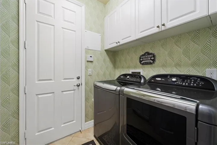 Laundry room with wallpapered walls, cabinet space, light tile patterned flooring, and washing machine and clothes dryer