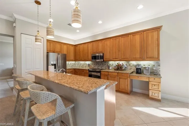 Kitchen featuring light tile patterned floors, decorative backsplash, appliances with stainless steel finishes, hanging light fixtures, and ornamental molding