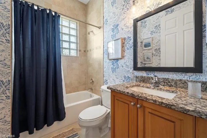 Full bathroom featuring wallpapered walls, shower / bath combination with curtain, and vanity