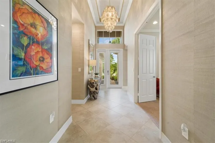 Hallway with french doors, crown molding, a chandelier, wallpapered walls, and light tile patterned flooring