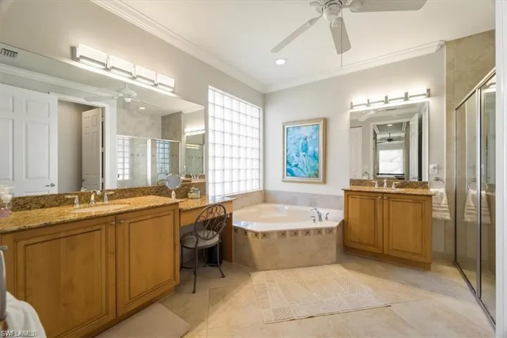 Full bathroom featuring a stall shower, ceiling fan, two vanities, a bath, and ornamental molding