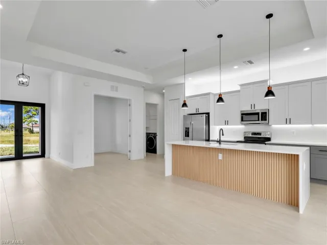 Kitchen with a tray ceiling, a spacious island, pendant lighting, stainless steel appliances, and recessed lighting