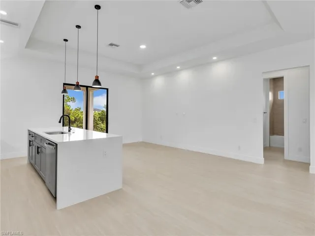 Kitchen featuring a raised ceiling, decorative light fixtures, light stone countertops, light wood finished floors, and recessed lighting