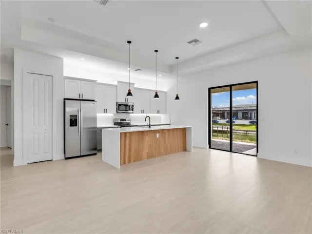 Kitchen featuring a raised ceiling, appliances with stainless steel finishes, a kitchen island with sink, pendant lighting, and open floor plan