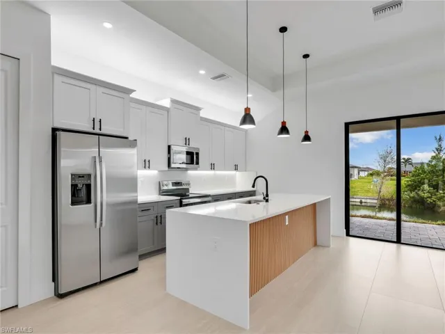 Kitchen featuring appliances with stainless steel finishes, pendant lighting, recessed lighting, light stone countertops, and an island with sink