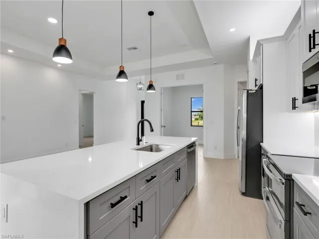 Kitchen featuring a raised ceiling, gray cabinetry, hanging light fixtures, stainless steel appliances, and recessed lighting