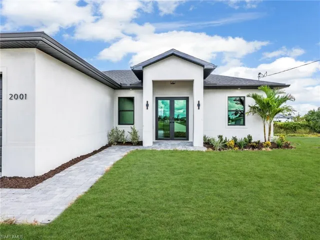 View of exterior entry featuring stucco siding, french doors, a lawn, and a shingled roof