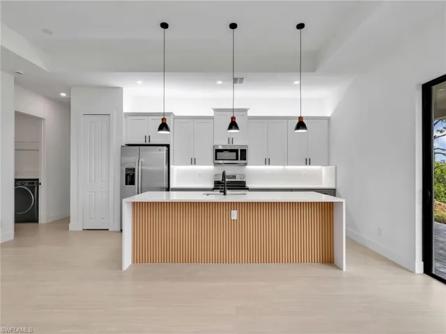 Kitchen with an island with sink, light stone countertops, decorative light fixtures, and recessed lighting