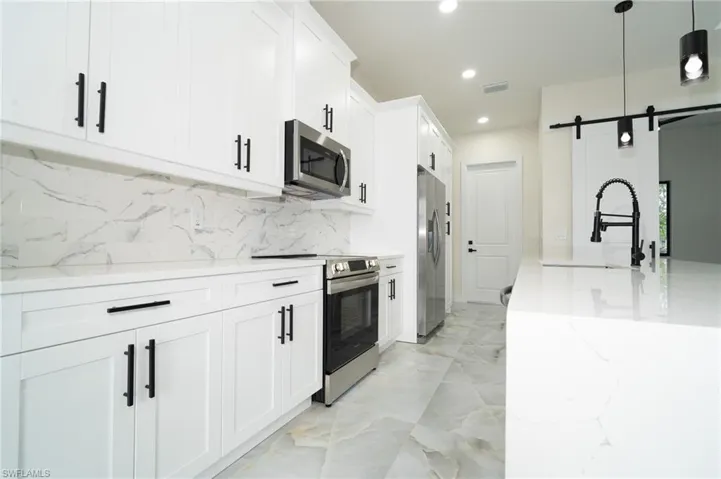 Kitchen with light stone countertops, appliances with stainless steel finishes, white cabinetry, hanging light fixtures, and a barn door