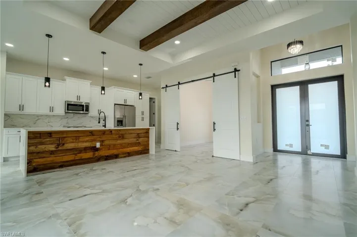 Kitchen with pendant lighting, appliances with stainless steel finishes, a barn door, a kitchen island with sink, and beamed ceiling