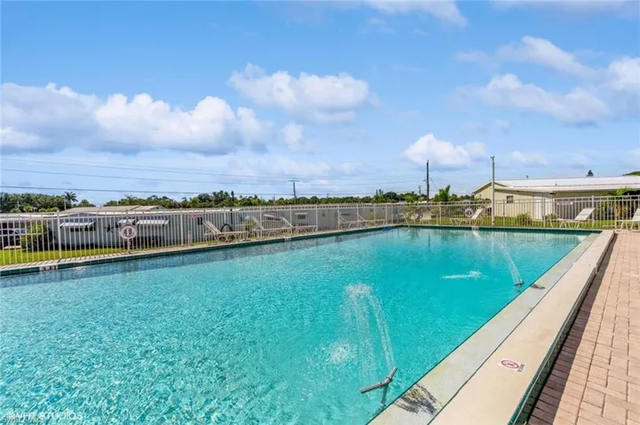 Rectangular heated swimming pool with water features, surrounded by a white perimeter fence and a paver deck