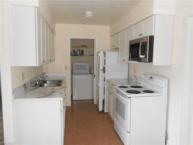 Kitchen with electric range, stainless steel microwave, washer / dryer, white cabinetry, and light tile patterned floors