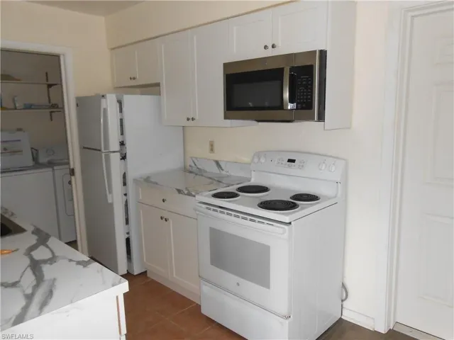 Kitchen with white appliances, white cabinets, washing machine and clothes dryer, and light tile patterned floors