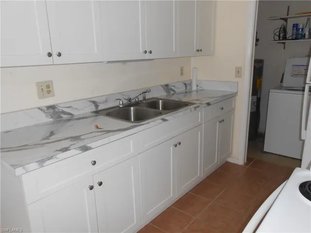Kitchen featuring light countertops, white cabinetry, light tile patterned flooring, and washer / dryer