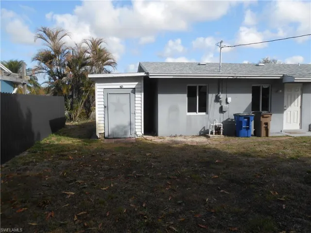 Rear view of house featuring roof with shingles and a storage shed