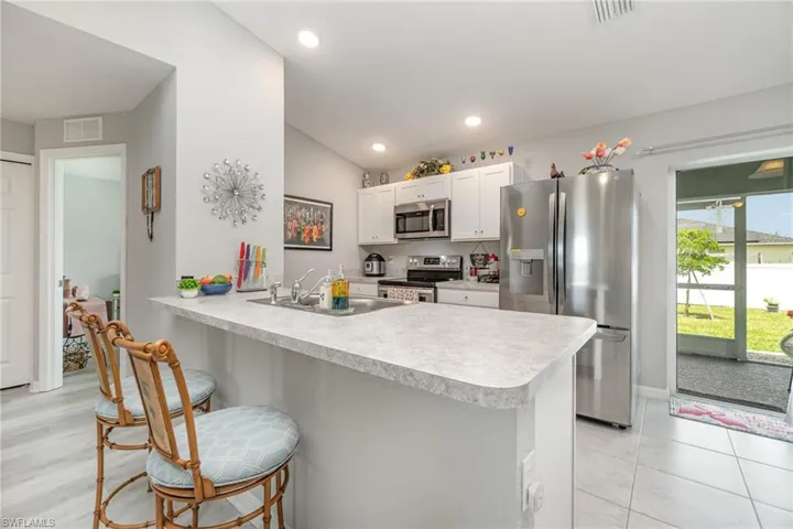 Kitchen featuring kitchen peninsula, lofted ceiling, white cabinets, sink, and appliances with stainless steel finishes