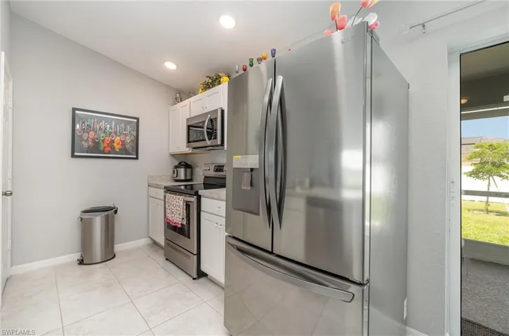 Kitchen featuring light tile flooring, white cabinetry,  appliances with stainless steel finishes, pantry closet  and lofted ceiling