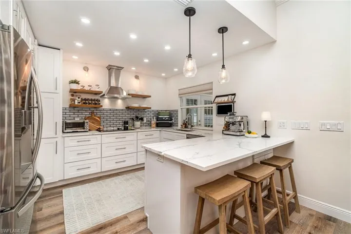 GORGEOUS Kitchen featuring stainless steel fridge, a peninsula, wall chimney range hood, open shelves, and light quartz countertops