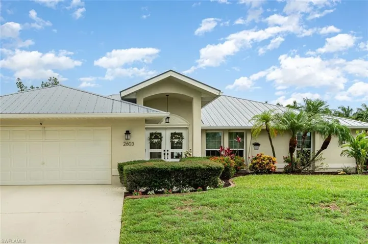 View of front facade featuring metal roof, stucco siding, driveway, and a front lawn