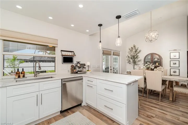 Kitchen featuring stainless steel dishwasher, a sink, a peninsula, hanging lights, and light LVP wood-type flooring