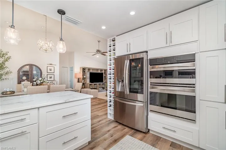 Kitchen featuring stainless steel appliances, white cabinets, a ceiling fan, light LVP wood-style flooring, and light stone countertops