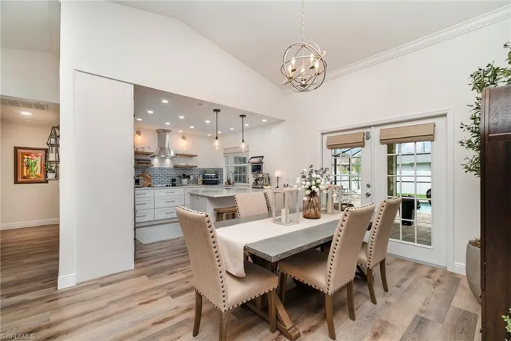 Dining room featuring a chandelier, light LVP wood-type flooring, french doors, baseboards, and high vaulted ceiling