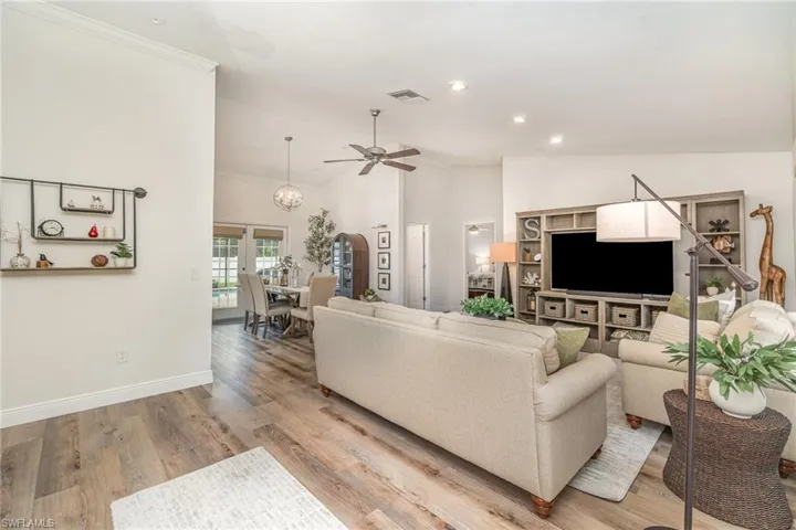 Living room featuring ceiling fan, vaulted ceiling, light LVP wood-style floors, crown molding, and baseboards