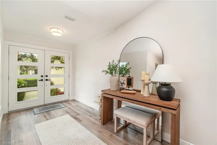 Foyer entrance with french doors, light LVP wood-style floors, baseboards, and crown molding