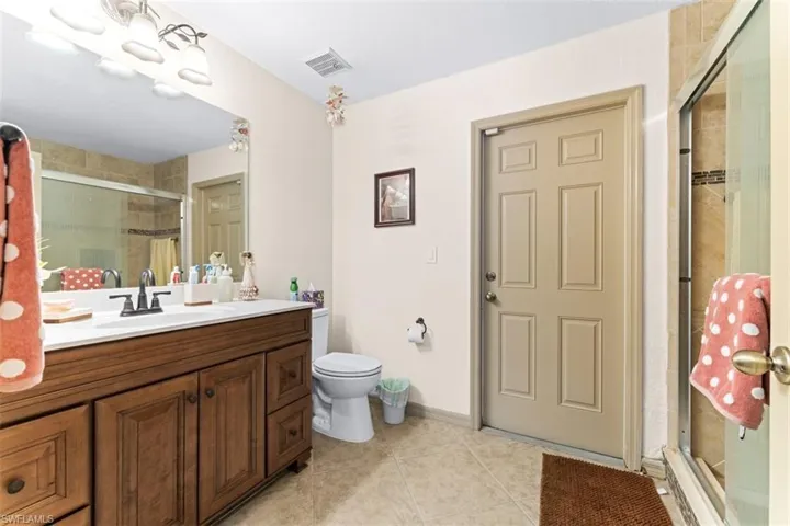 Bathroom featuring a dark wood-finish vanity with a white countertop and rectangular sink, a glass-enclosed shower with tiled walls and decorative accent band, and tiled flooring