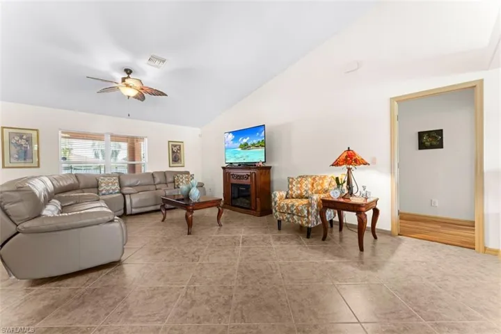 Living room featuring neutral-toned tile flooring, vaulted ceilings, and a ceiling fan with integrated lighting