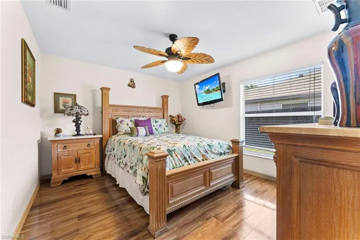 Bedroom featuring wood-finish flooring, a ceiling fan with integrated lighting, and a window with horizontal blinds