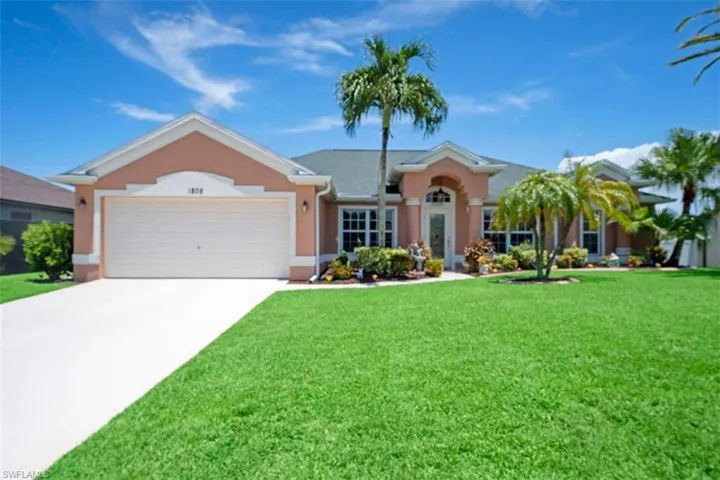 Stucco exterior with a peaked roofline, an attached two-car garage, a concrete driveway, and mature palm trees