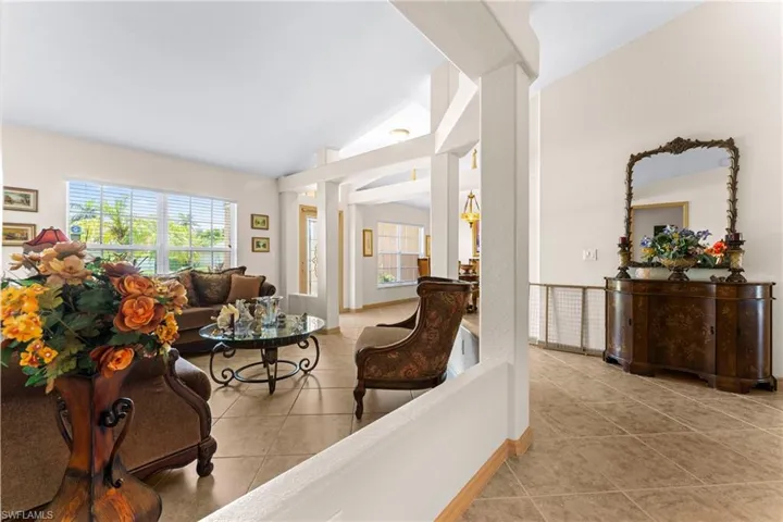 Spacious living area featuring vaulted ceilings, tile flooring, large windows with blinds, and architectural columns