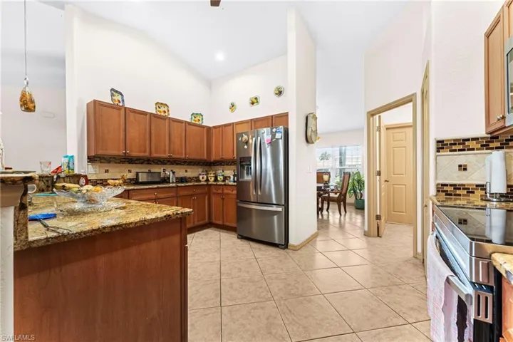 Kitchen featuring wood cabinetry, stainless steel refrigerator, granite countertops, tile backsplash, and tile flooring