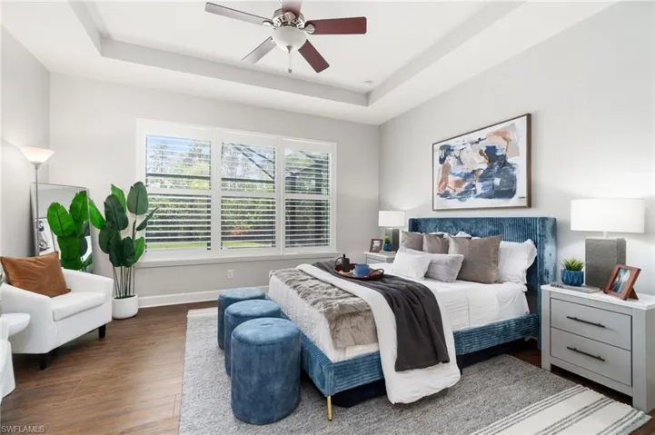 Primary bedroom resides on the first floor, In a separate wing overlooking the saltwater pool & featuring ceiling fan, a raised ceiling, and dark wood-type flooring