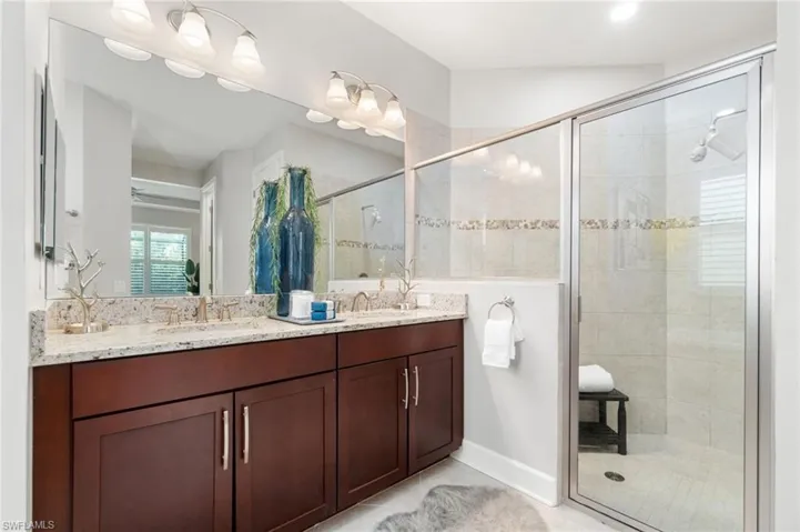 Glass shower enclosure and dual bowl vanity highlighted by gold fixtures and light granite counters