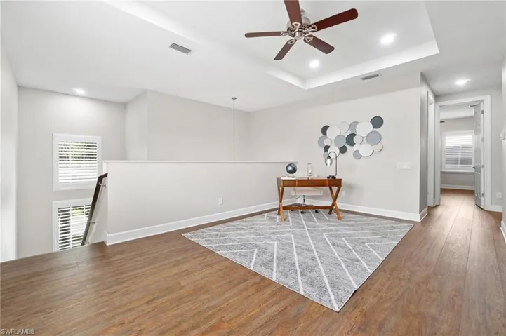 Upstairs loft area with ceiling fan, a raised ceiling, and hardwood / wood-style floors.  No carpet upstairs or anywhere in the home.
