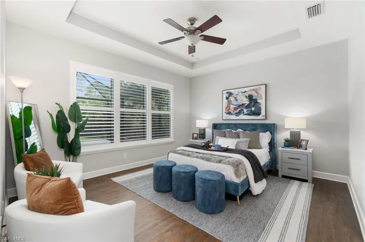 Spacious primary bedroom features dark hardwood / wood-style floors, a raised ceiling, and ceiling fan, and plantation shutters
