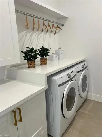 Laundry room with light tile patterned flooring, washing machine and clothes dryer, and cabinets