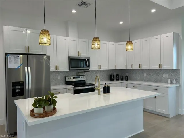 Kitchen with hanging light fixtures, white cabinets, a center island with sink, and stainless steel appliances